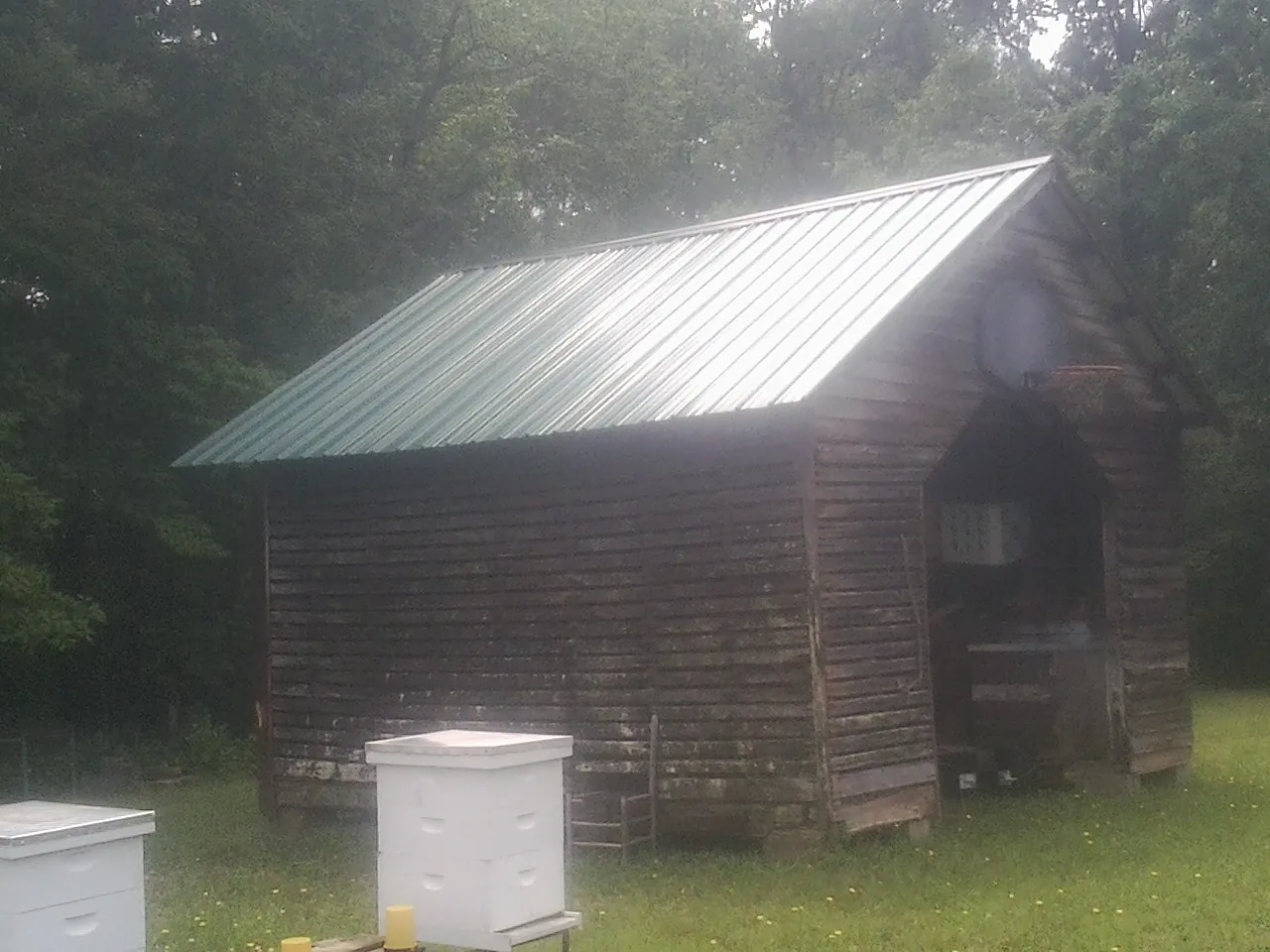 Green metal roof on a weathered barn beside stacked beehives in Empire