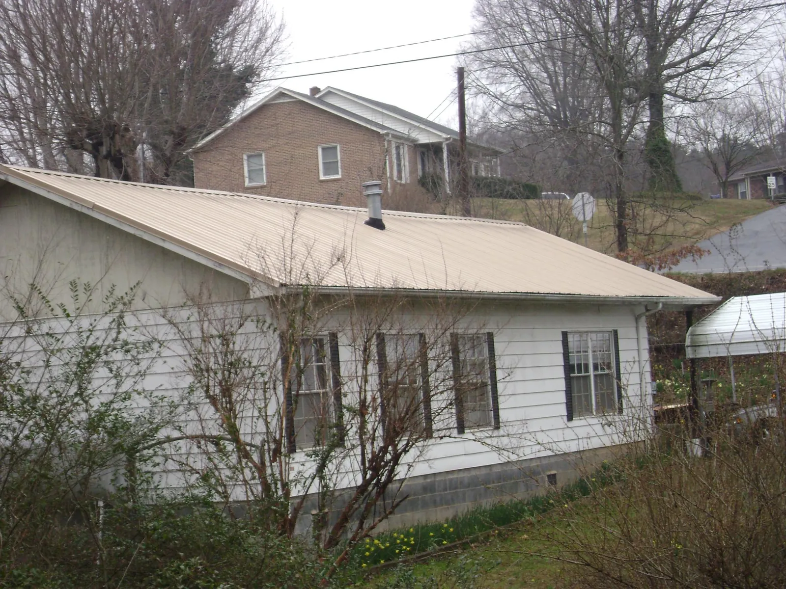 Tan metal roof on a white sided house set into a hillside — Commercial Roofing by Roofing Brothers in Empire